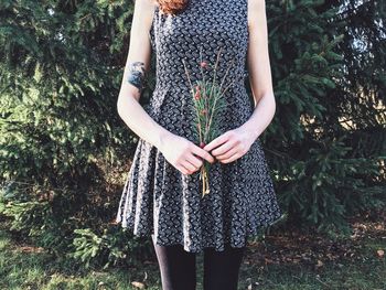 Midsection of woman holding flowers against trees