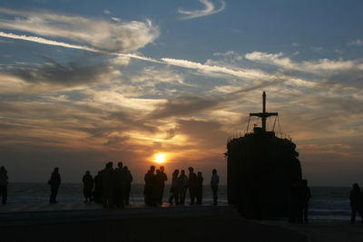 Silhouette people on beach against sky during sunset