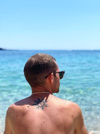 Rear view of shirtless man sitting at beach against clear sky