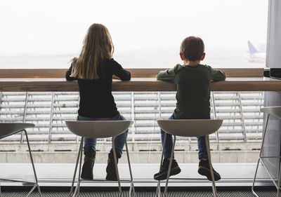 Rear view of siblings sitting on seats by window in restaurant