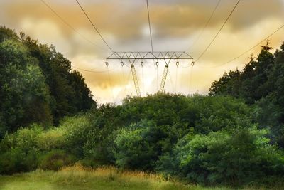 Electricity pylon by trees against sky during sunset