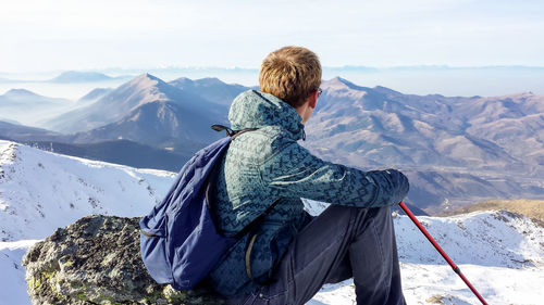 Rear view of man sitting on rock at mountain