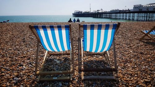 Deck chairs on beach against sky