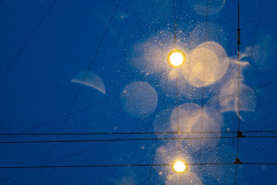 Low angle view of illuminated lighting equipment against blue sky