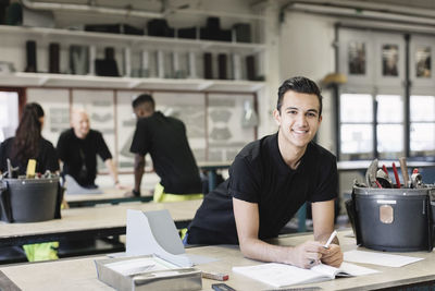 Portrait of smiling male mechanic at table with coworkers in background