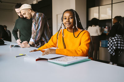 Portrait of smiling woman with braided hair studying by friends discussing in community college