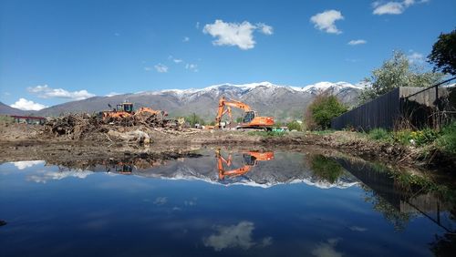 Construction vehicle by lake against blue sky