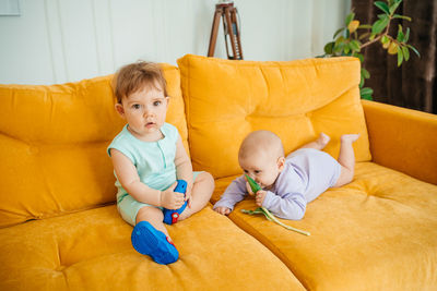 Two babies playing on a yellow sofa