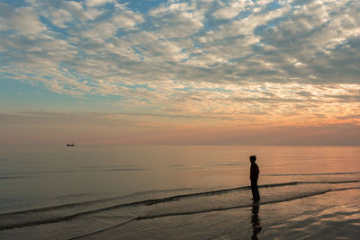 A boy on a beach standing and watching the boat