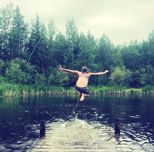 Full length of man jumping in lake against sky