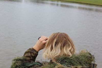 Rear view of woman looking through binoculars against lake