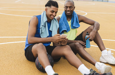 Son sharing mobile phone with father sitting on basketball court