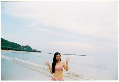 Portrait of woman gesturing while standing at beach against sky