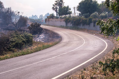 Empty road by trees in city against sky