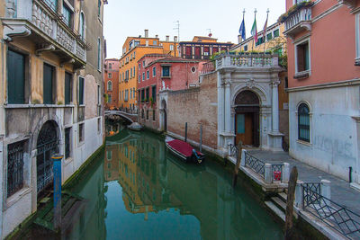 Boats moored in canal by city against sky