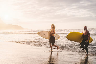 Shirtless men carrying surfboards while walking at beach