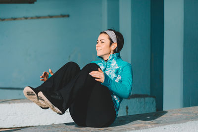 Side view of smiling young woman sitting on retaining wall