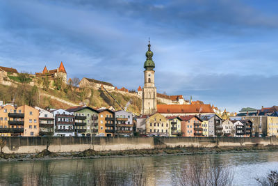 Buildings at waterfront against cloudy sky