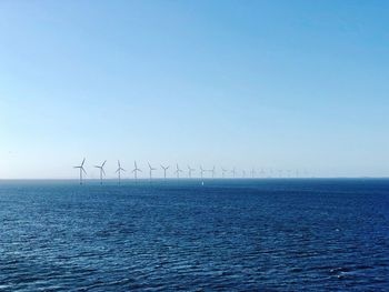 Windmills in sea against clear blue sky