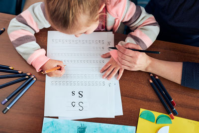 Little girl preschooler learning to write letters with help of her mother. kid writing letters