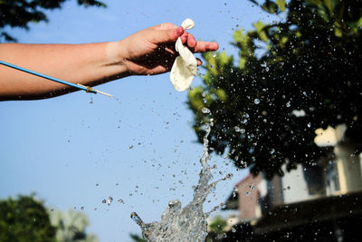 Cropped hand bursting water bomb against clear sky