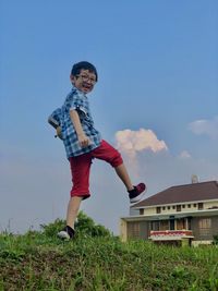 Full length of smiling boy standing on grass against sky