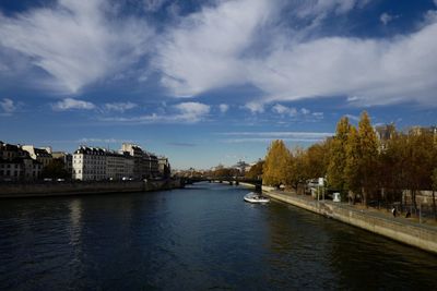 View of buildings by river against cloudy sky