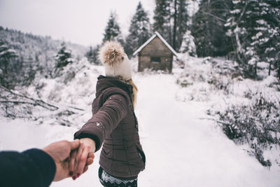 Woman looking at cottage against trees during winter