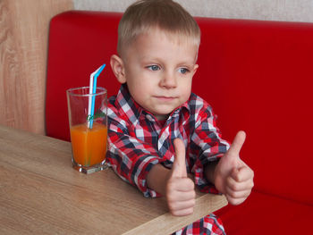 Cute boy gesturing thumbs up sign while sitting by juice at restaurant