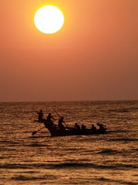 Silhouette people in sea against sky during sunset