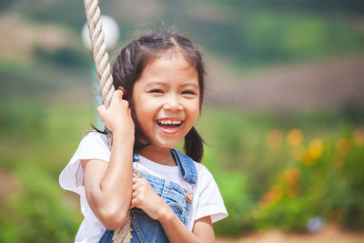 Cheerful girl swinging on rope swing at playground