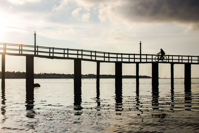 Man riding bicycle on pier over lake against sky