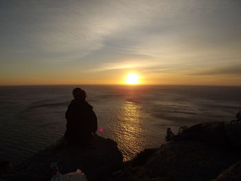 People looking at sea against sky during sunset