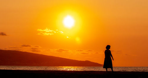 Woman dancing at beach, watching the sunset, silhouette.