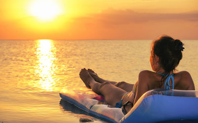 Young woman wear bikini lies on inflatable mattress on sunset orange background  sea rest sun tan