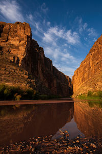 Rock formations by lake against sky