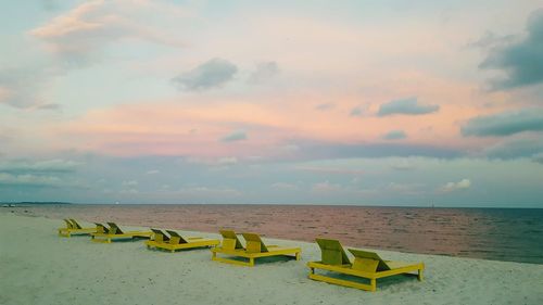 Lounge chairs on sea shore against sky during sunset