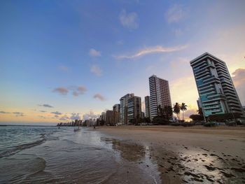 Sea by buildings against sky during sunset