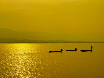 Silhouette people on boat in sea against sky during sunset