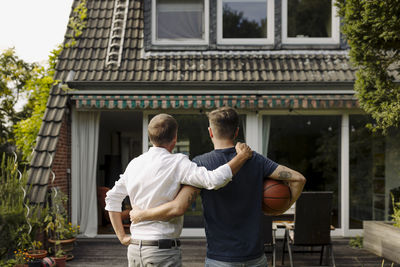 Father and son with arm around standing in front of house