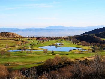 Scenic view of field by lake against sky