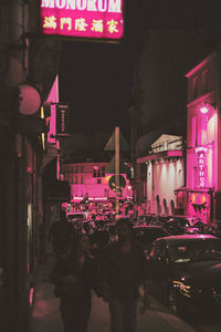 People on road against illuminated buildings in city at night