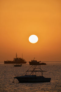 Silhouette ship in sea against orange sky