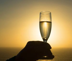 Close-up of beer glass against sunset sky