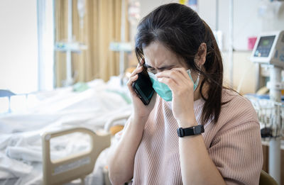 Crying woman wearing mask talking on phone at hospital