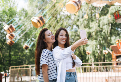 Young women with long hair friends having fun taking selfie on mobile phone at amusement park