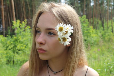 Close-up of thoughtful young woman wearing flowers while standing in park