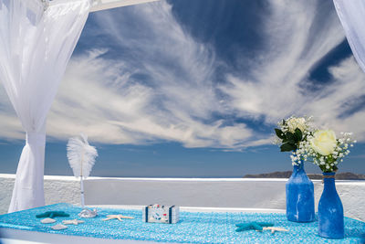 Flower vases on table at santorini against cloudy sky during sunny day