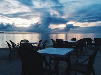 Empty chairs and tables by sea against sky