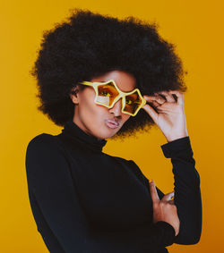 Young man wearing sunglasses standing against yellow background